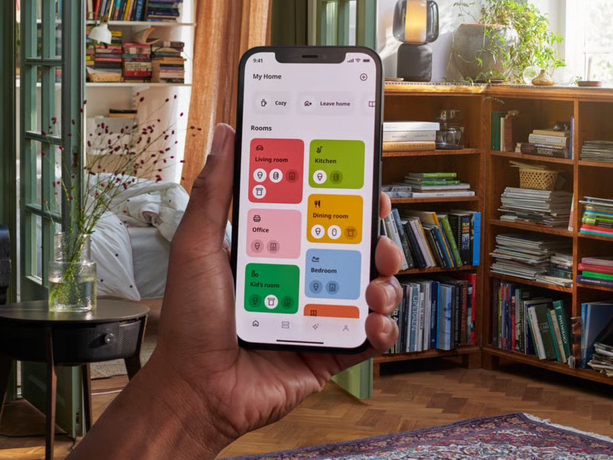 The IKEA Dirigera hub, a small white device with a simple design, is displayed on a table, with a smartphone and a smart light bulb nearby, showcasing the device's ability to connect and control various smart home products in the UK