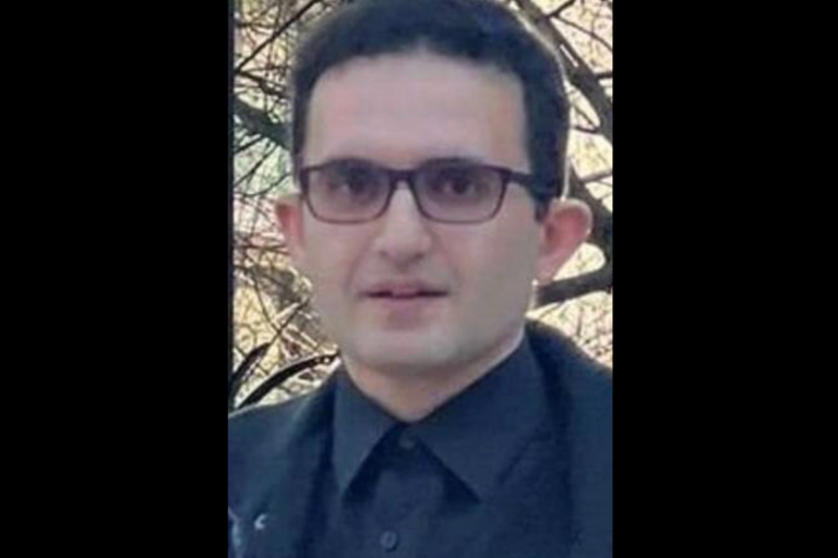 A photograph of a candlelit vigil for the Canadian activist, with a background of Iranian flags and protest signs, highlighting the global response to the targeted killing and the ongoing struggle for human rights and democracy