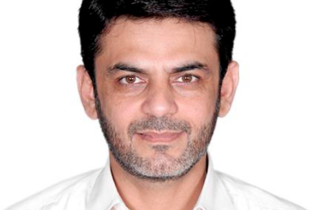 A photo of a person in a suit, with a serious expression, in front of a US flag, symbolising the US political assassination plot and the alleged involvement of the Revolutionary Guard, with a colour palette of red, white, and blue, representing the US and its values.