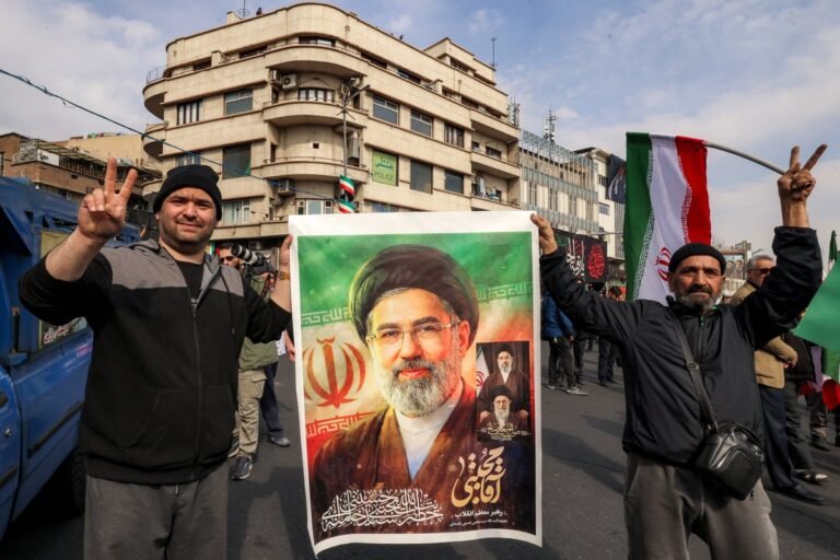 Iran's new supreme leader stands proudly in front of a Iranian flag, symbolising the country's resistance to US influence and its commitment to maintaining its independence and sovereignty, with a strong and determined expression on his face, surrounded by his supporters and advisors, in a powerful and emotive image that captures the mood of the nation