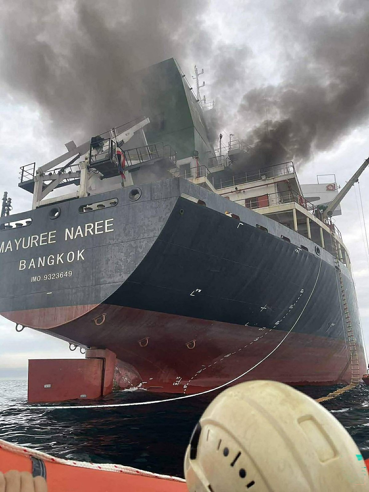 A cargo ship navigating through the Strait of Hormuz, with the Iranian coastline in the background, highlighting the importance of this critical waterway for international trade and the potential risks of conflict in the region