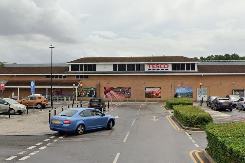 A Tesco store with a sign indicating increased security measures, highlighting the primary keyword of supermarket safety and the need for retail security to prevent customer abuse and vehicle attacks