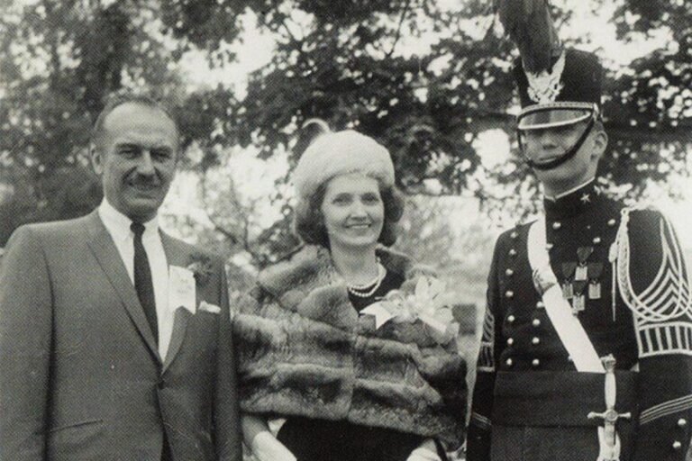 Donald Trump sitting in the Oval Office, surrounded by American flags and military personnel, with a picture of his parents on his desk, symbolising his admiration for the American military and its dominance, a topic of significant interest and discussion