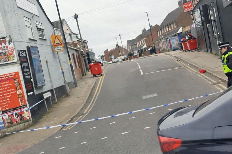 Police officers sealing off a road in Birmingham after a man was hurt in an early-morning disorder, with a police car and tape blocking the road, as people watch from a distance, highlighting the importance of public safety and community cohesion