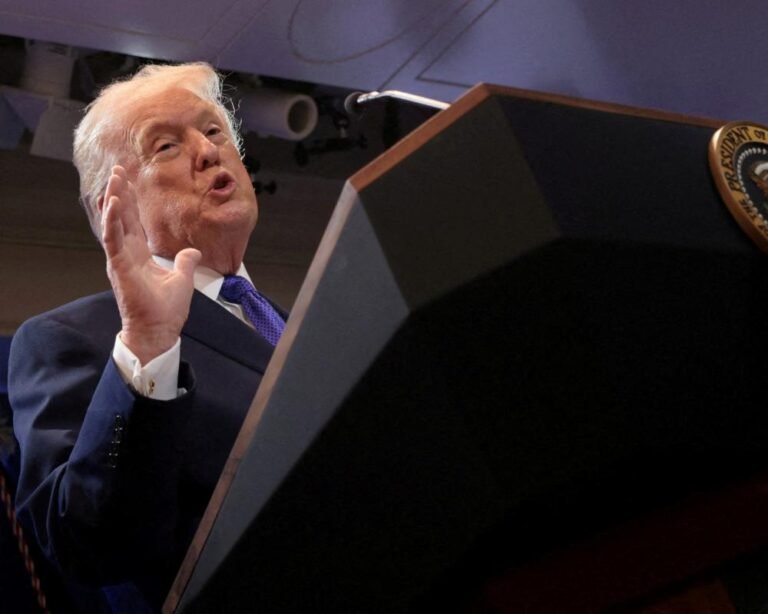 Donald Trump speaking at a press conference, surrounded by reporters, with a serious expression, discussing his tariff policies and their impact on global trade, as the US flag waves in the background, symbolising his 'America First' agenda