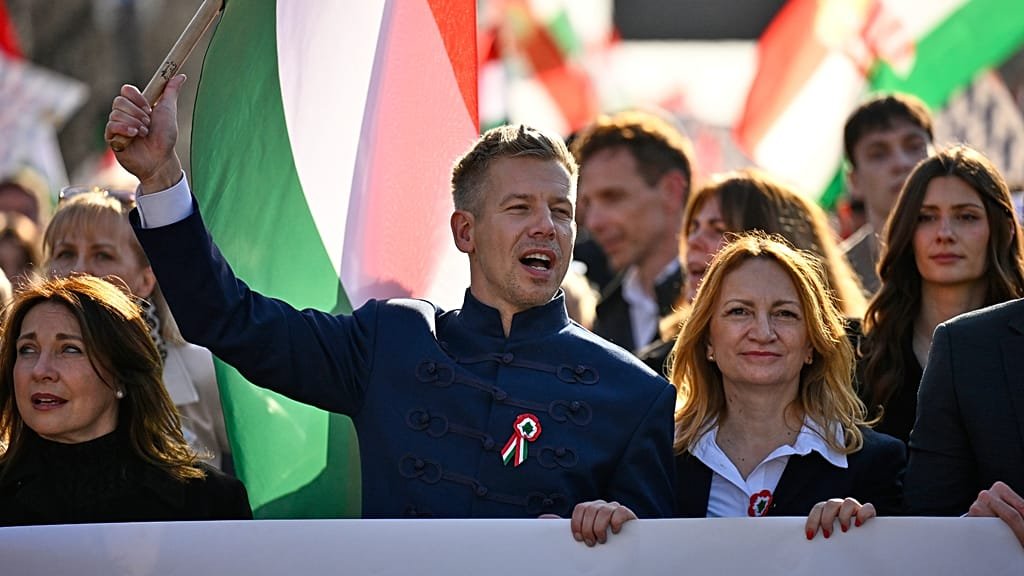 A protest in Budapest, Hungary, with people holding signs that read 'Democracy' and 'Freedom' as they march against the alleged betrayal of Hungarian freedom by Prime Minister Viktor Orbán, who has been accused of inviting Russian agents to interfere with the country's voting system, highlighting the threat to democratic institutions and the rule of law in the country