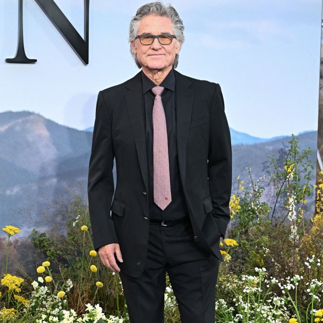 Kurt Russell smiling and holding a cake with candles, surrounded by his family and friends, celebrating his 75th birthday in style, with a huge birthday cake and colourful decorations, highlighting his remarkable film career and legacy as a Hollywood legend
