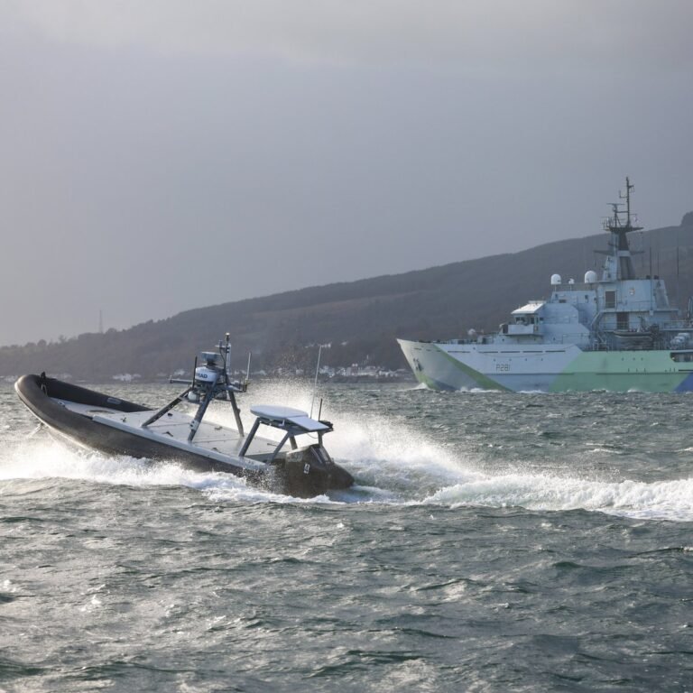 A Royal Navy Type 45 destroyer and sea drones escorting tankers through the Strait of Hormuz, with the Iranian coastline in the background, highlighting the importance of the Royal Navy's deployment in maintaining stability in the region and protecting British interests