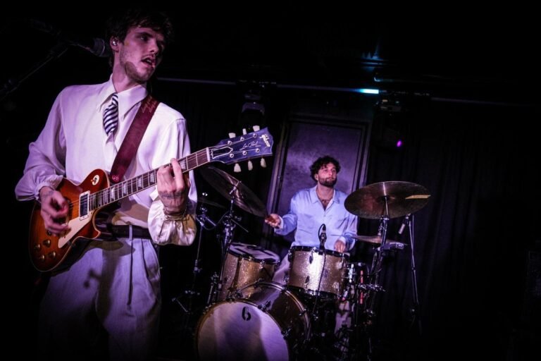 Cruz Beckham and The Breakers performing live on stage, with a crowd of enthusiastic fans in the background, all enjoying the music and energetic atmosphere, with a focus on the band's unique sound and style