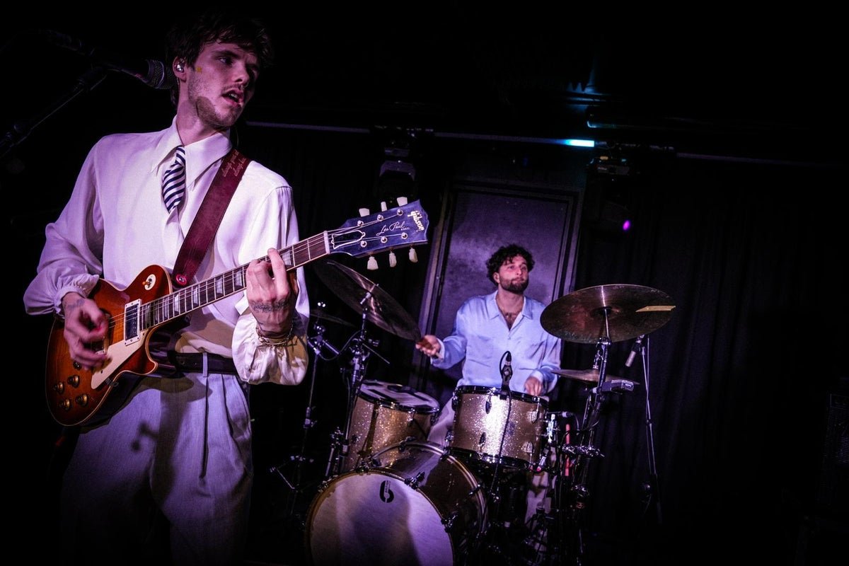 Cruz Beckham and The Breakers performing live on stage, with a crowd of enthusiastic fans in the background, all enjoying the music and energetic atmosphere, with a focus on the band's unique sound and style