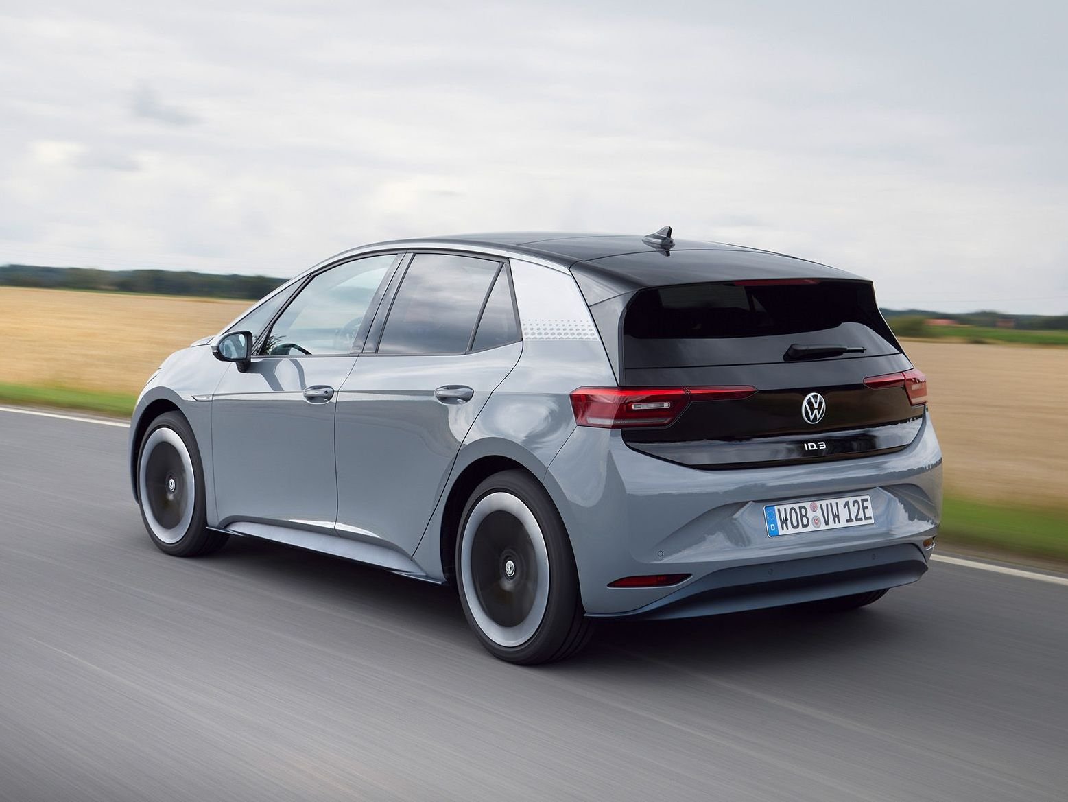 A used electric vehicle charging at a public charging point in the UK, with a person in the background looking at their phone, highlighting the increasing demand for used EVs as fuel costs rise