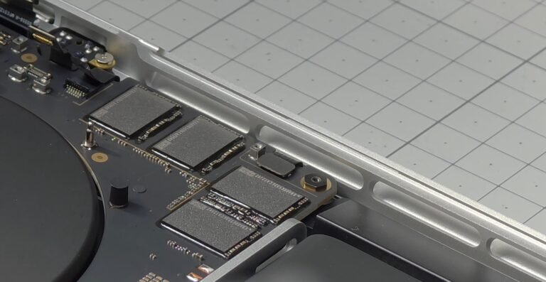 A close-up of the M5 Max MacBook Pro's SSD, with a thermometer showing a temperature of over 100 degrees Celsius, highlighting the severe heat issue in the UK