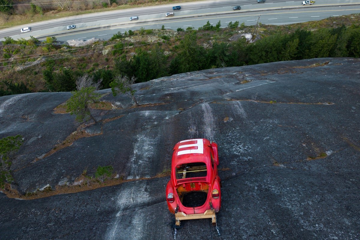 A car suspended on a rock face, with authorities warning the public to stay away due to safety concerns and potential environmental damage, highlighting the importance of responsible behaviour and environmental conservation