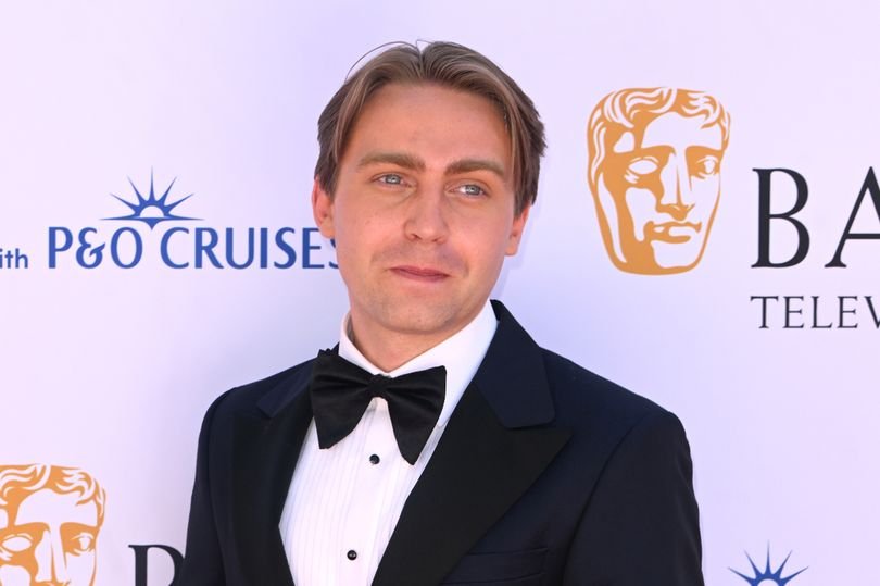 Barney Walsh, the host of BBC Gladiators, standing in front of a car with a sombre expression, highlighting the importance of responsible driving and the consequences of reckless behaviour on the road, a key aspect of his personality and public image