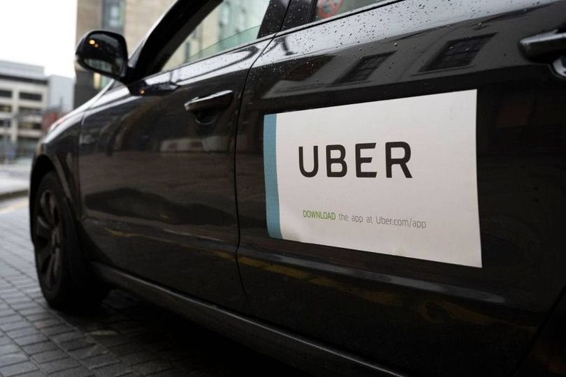 A woman standing alone at a bus stop in Birmingham, looking concerned and frightened after her encounter with the thief in the stolen Uber, with a blurred image of the Uber in the background, highlighting the importance of safety and security in ride-hailing services