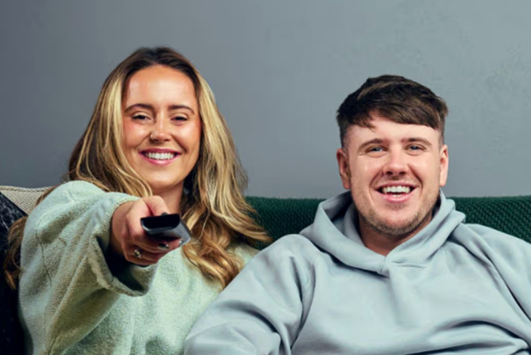 Gogglebox couple sitting on a couch, looking sad and shocked, with a TV in the background, featuring the popular Channel 4 series, with a focus on the couple's behaviour and relationship