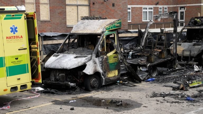 A London ambulance parked outside a hospital, with a group of people gathered nearby, discussing the recent false flag claim made by a London Green candidate, which has sparked outrage and controversy in the community, highlighting the need for accurate information and responsible behaviour