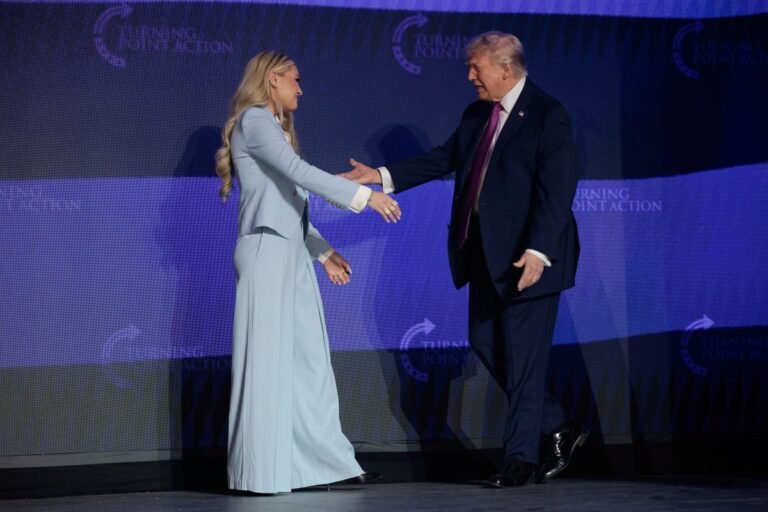 Erika Kirk standing on stage with Donald Trump at the Turning Point rally, with a crowd of people in the background, as she introduces him amidst a flurry of security concerns and controversy surrounding her recent decision to skip a Vance event due to serious threats, with her behaviour and priorities under scrutiny