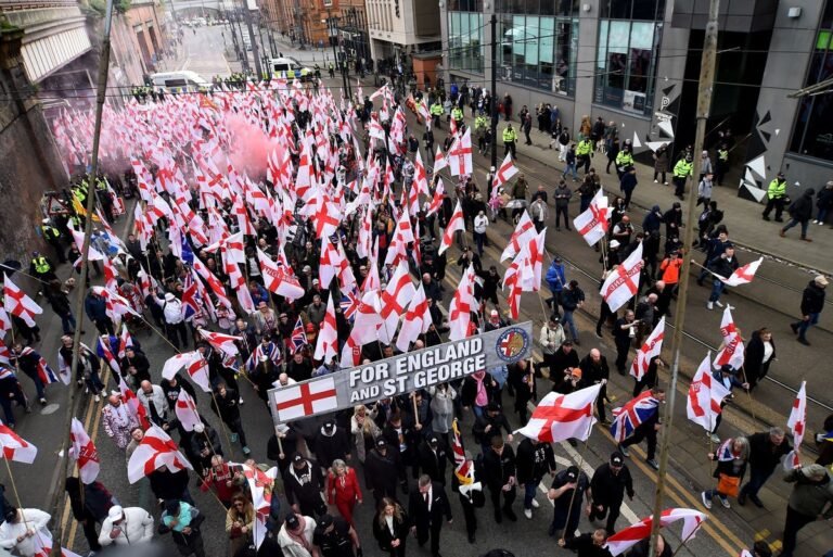 A crowd of protesters and counter-protesters gather in Manchester, with police officers visible in the background, as the city experiences a surge in demonstrations related to Britain First and free speech