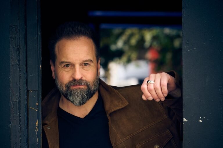 Alfie Boe, a British tenor, stands on stage, looking out at the audience with a powerful expression, symbolizing his journey of self-forgiveness and mental health awareness