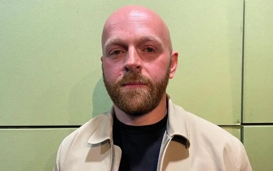 A Morrisons store front with a sign reading 'shoplifting is a crime' and a security guard standing outside, highlighting the company's approach to retail crime and shoplifting