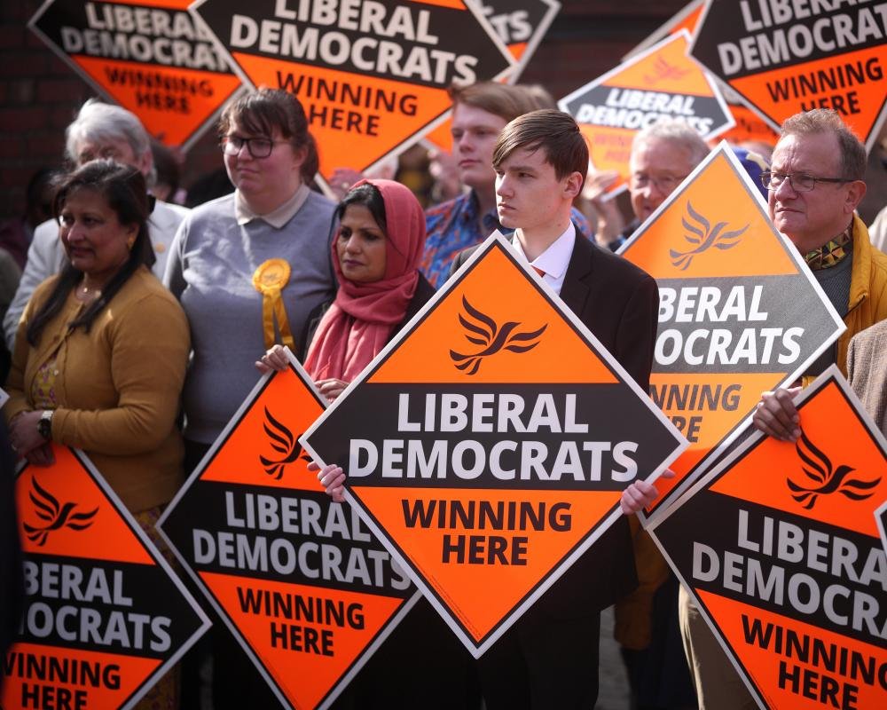 A group of Liberal Democrat councillors gathered around a table, discussing local issues and policies with a focus on sustainability and community development, highlighting the party's commitment to transparency and accountability
