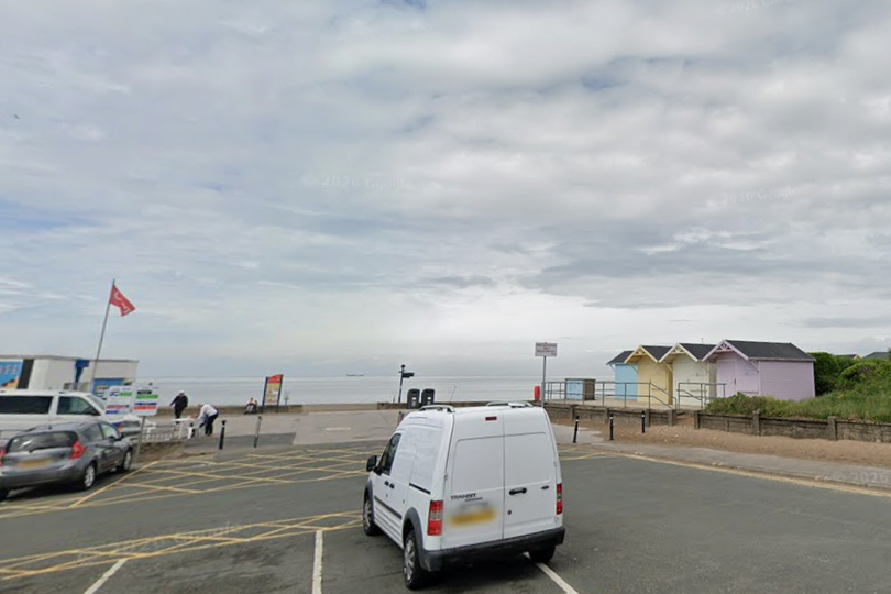 A woman walking her dog along a seaside path, with a stunning view of the sea in the background, highlighting the importance of safety and responsible behaviour in such areas