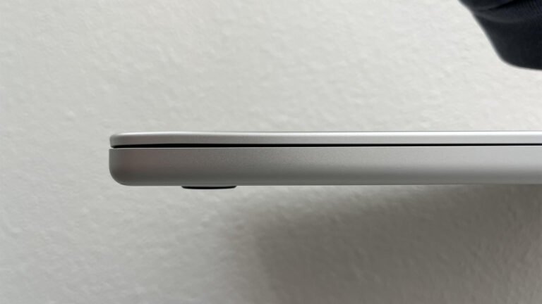 A person holding a MacBook at a UK airport security checkpoint, with a concerned expression, highlighting the importance of laptop protection during travel