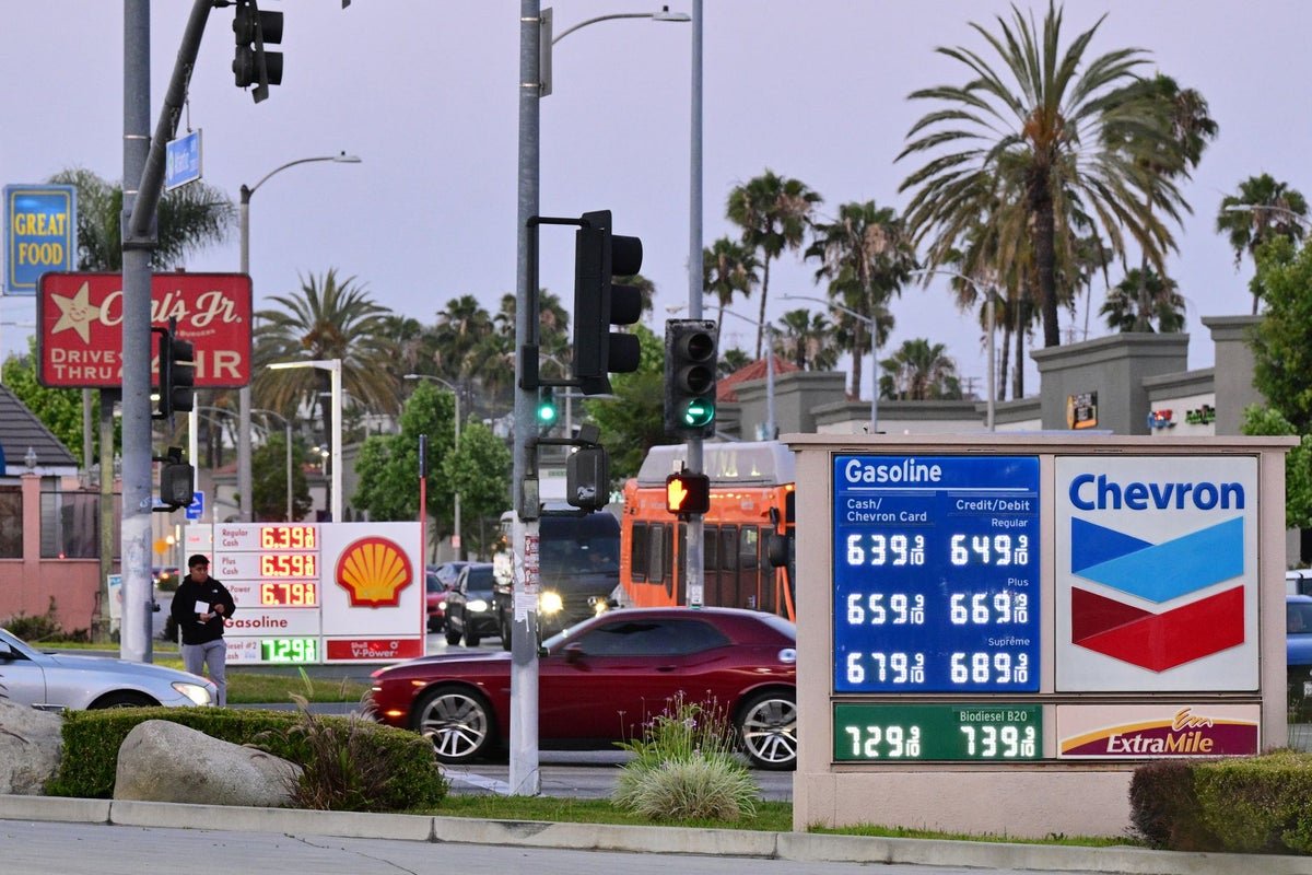 A close-up of a fuel pump with a worried driver in the background, highlighting the primary keyword of petrol prices and the impact on daily life