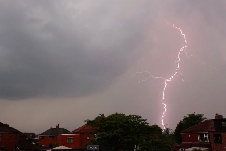 A dramatic image of a thunderstorm over the UK countryside, with dark clouds and lightning illuminating the sky, representing the primary keyword phrase UK weather