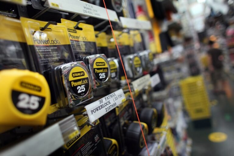 Stanley's iconic yellow tape measure on a workbench, with a foreign model in the background, symbolising the shift in demand and consumer preference for the overseas version, with a focus on the tool manufacturing industry