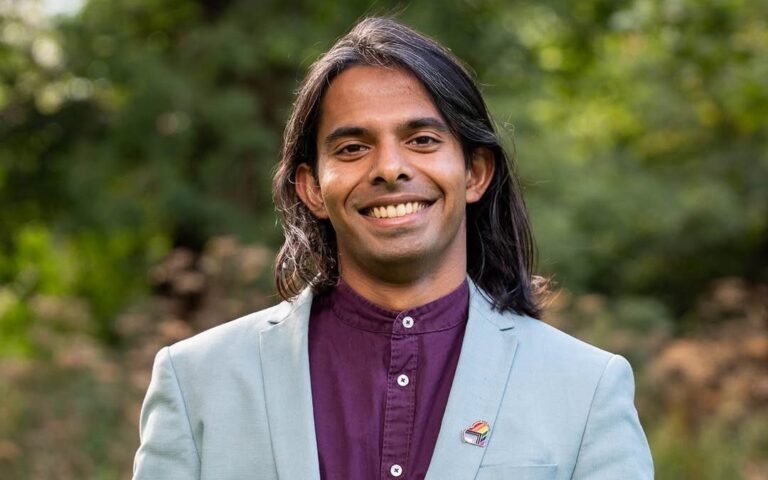 A photo of the Trans Green Party candidate standing in front of a Scottish flag, with a determined expression, highlighting their commitment to diversity and representation in Holyrood