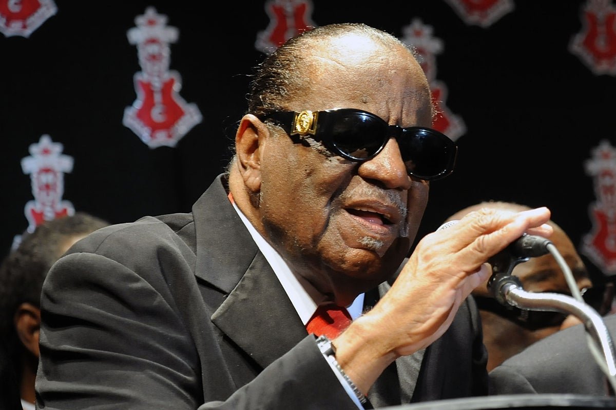 Clarence Carter performing on stage, singing his hit song Strokin, with a soulful voice and energetic behaviour, surrounded by colour and music