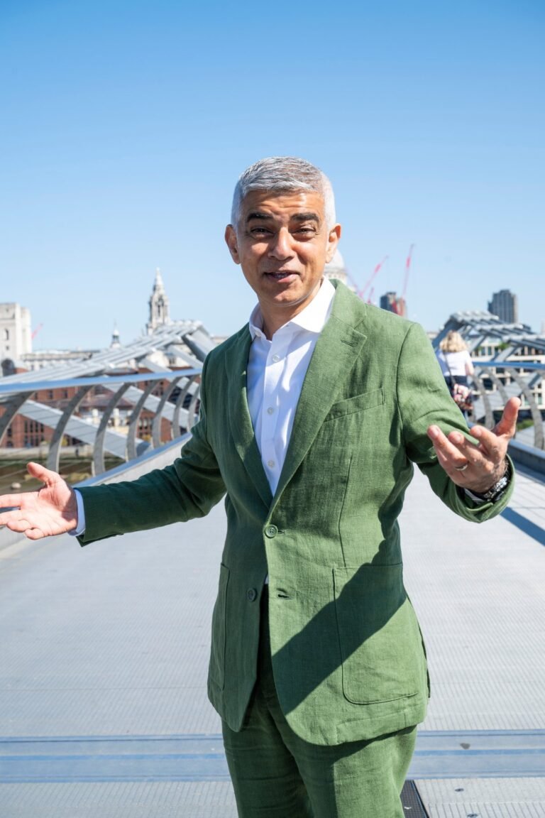 Sadiq Khan, the Mayor of London, standing in front of the London skyline, with a buses and bicycles in the foreground, highlighting his commitment to sustainable transport and reducing air pollution in the city