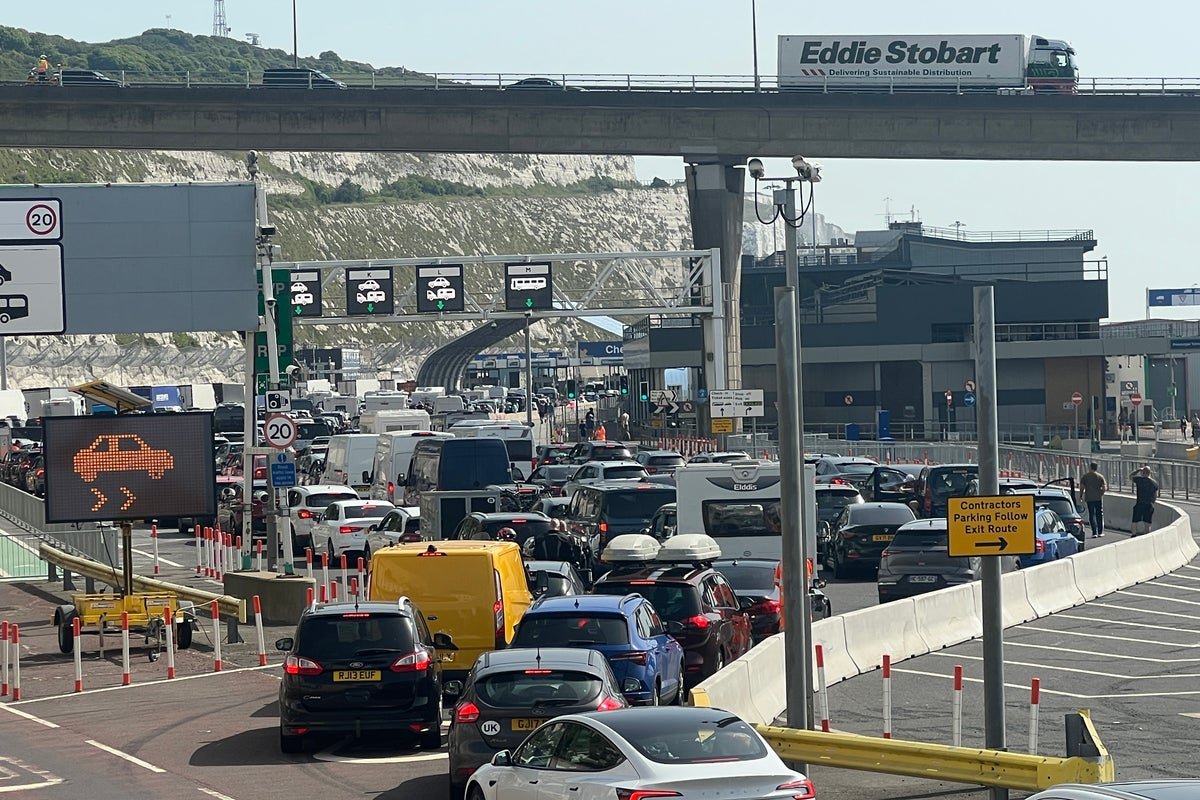 A queue of lorries at the Dover border crossing, with a customs officer checking documents. The scene is one of chaos and disruption, with lorries parked on the side of the road and drivers waiting patiently. The image highlights the need for a more efficient and effective entry-exit system, with advanced technology and streamlined processes to reduce delays and improve security. The primary keyword is entry-exit system