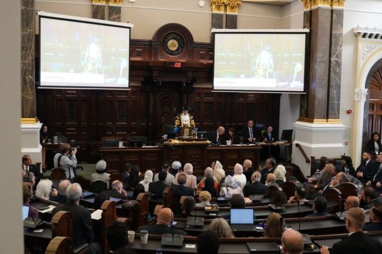 A group of people from different cultural backgrounds gathered around a table, engaged in a discussion, with a Birmingham council meeting room in the background, highlighting the importance of community relations and social cohesion in the city