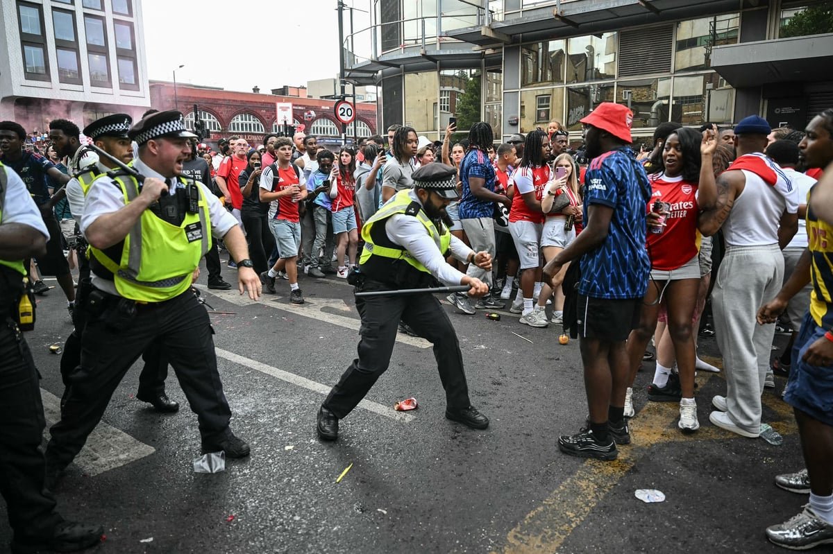 A descriptive image of the Arsenal trophy parade chaos, with a massive crowd and police presence, highlighting the need for increased safety measures and crowd control, as people behave in an unruly manner, with flares and smoke filling the air, and a hotel fire in the background
