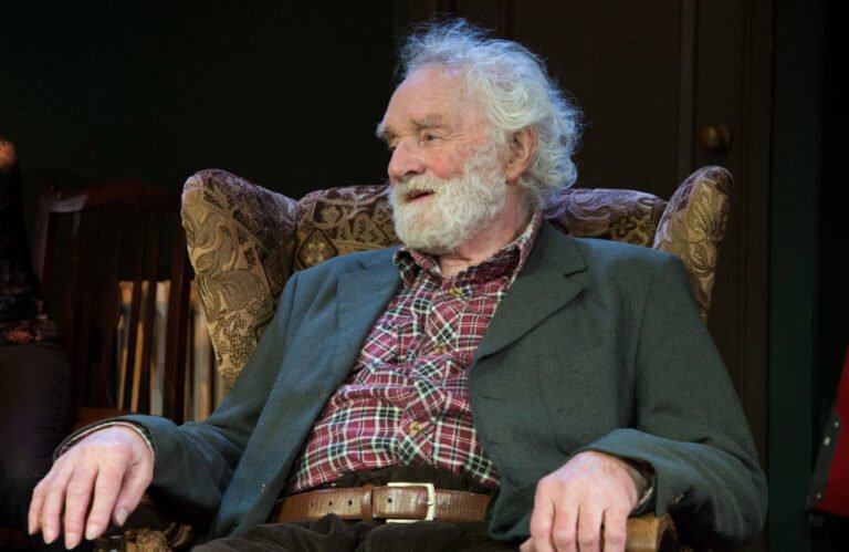 A photo of Patrick Godfrey on stage, in character, with a captivating expression, showcasing his exceptional acting abilities, a true legend in the entertainment industry, with a career spanning decades, and a lasting impact on the world of theatre and film