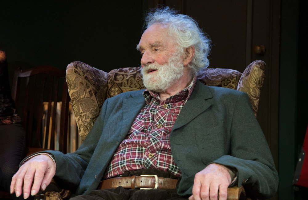 A photo of Patrick Godfrey on stage, in character, with a captivating expression, showcasing his exceptional acting abilities, a true legend in the entertainment industry, with a career spanning decades, and a lasting impact on the world of theatre and film