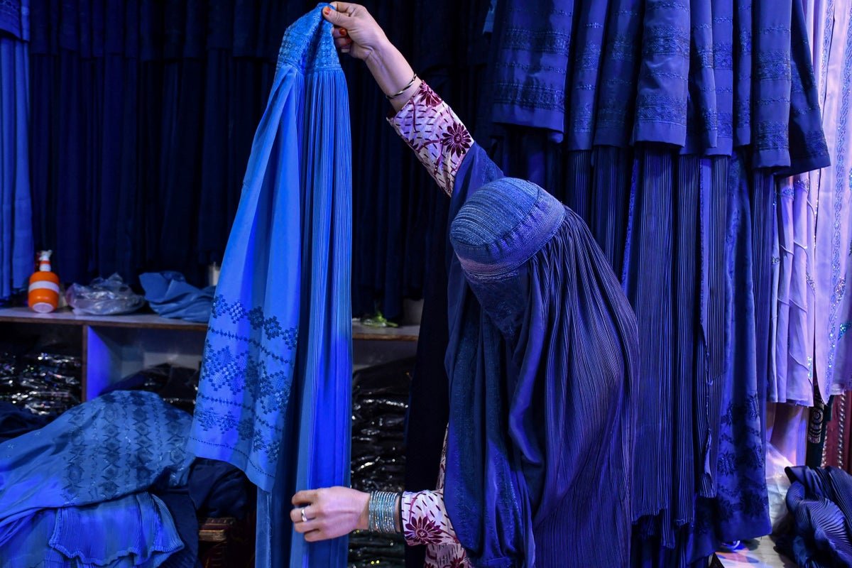 A woman in a burqa walks down a street in Afghanistan, with a subtle hint of defiance in her stride, as the Taliban's strict dress code continues to spark controversy and debate, with the primary keyword being Taliban dress code