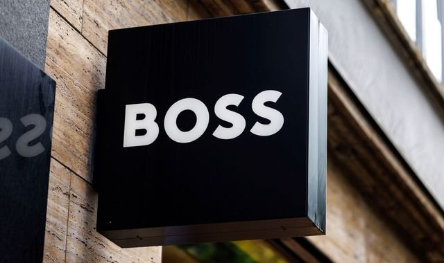 Frasers Group owner Mike Ashley outside a Sports Direct store, with a Hugo Boss store in the background, symbolising the potential takeover of the luxury fashion brand by the retail giant