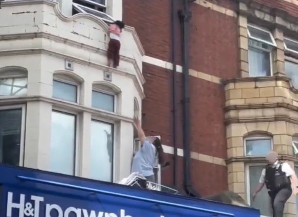 A child is rescued from a window ledge above a London high street shop, with a dramatic scene unfolding as witnesses watch in horror, the primary keyword being child rescue