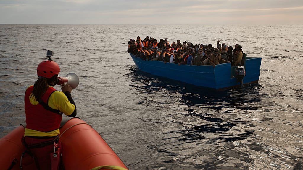 A group of migrants on a boat, with the European Union flag in the background, symbolising the EU's migration pact and its efforts to provide a more humane and coordinated response to migration