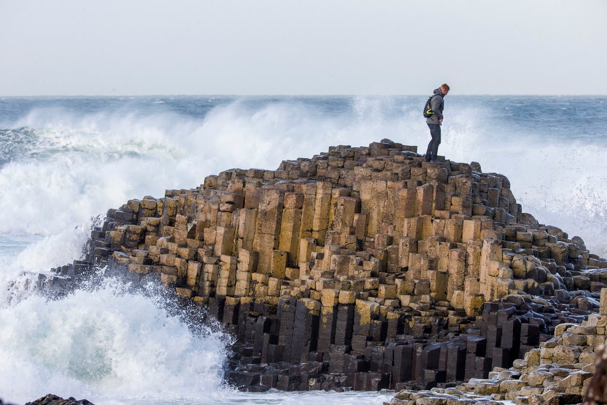 The Giant's Causeway, a natural wonder in Northern Ireland, featuring unique interlocking basalt columns, a result of intense geological forces, with a vibrant colour palette, ranging from deep blacks to vibrant oranges, against a backdrop of rugged coastline and dramatic skies